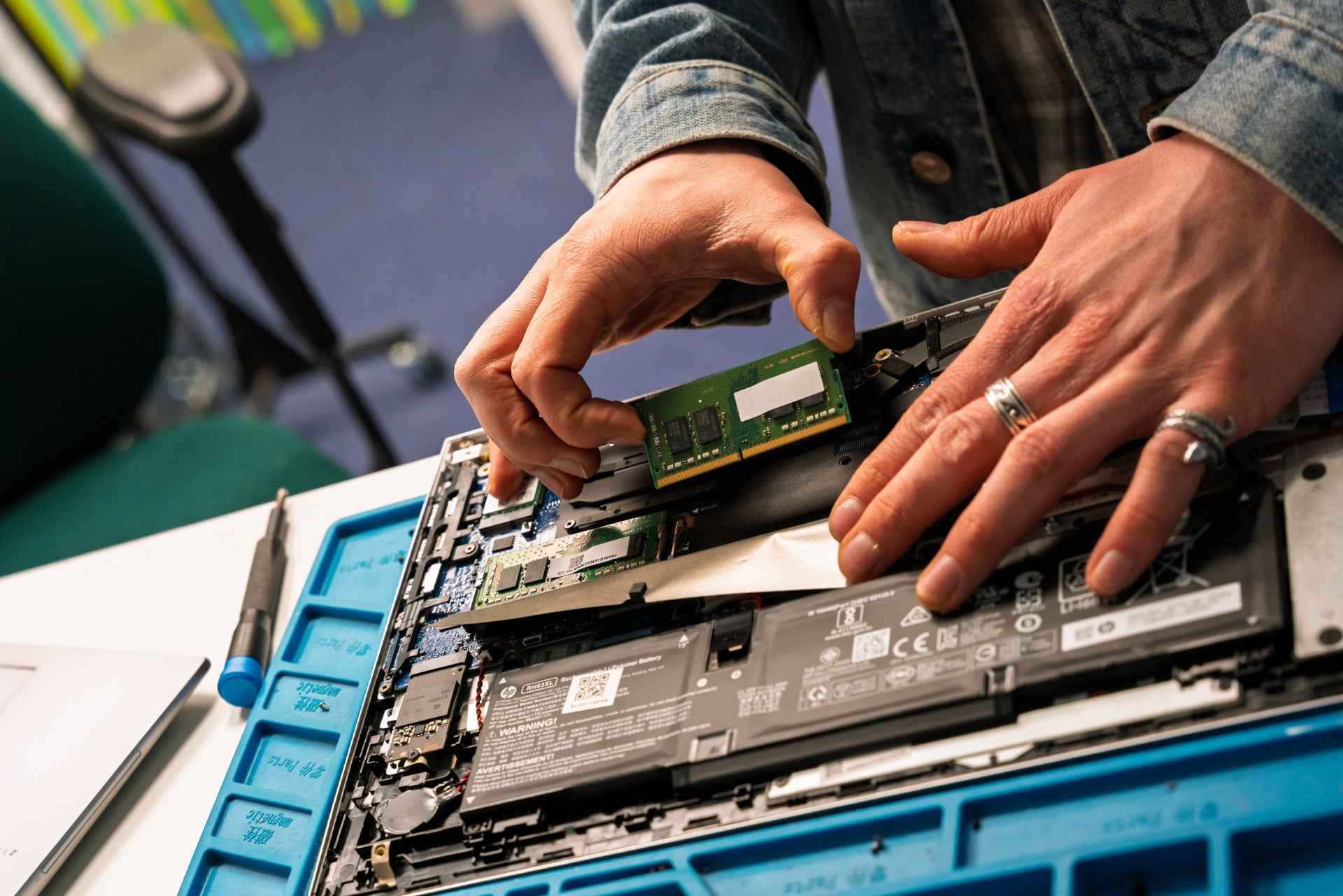 Person installing RAM into a laptop with tools on a blue mat